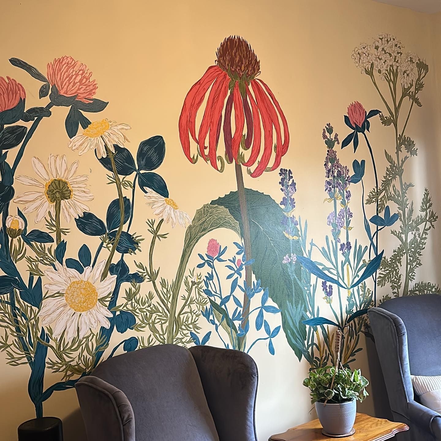 Floral mural on a tan wall with two gray armchairs and a small potted plant.
