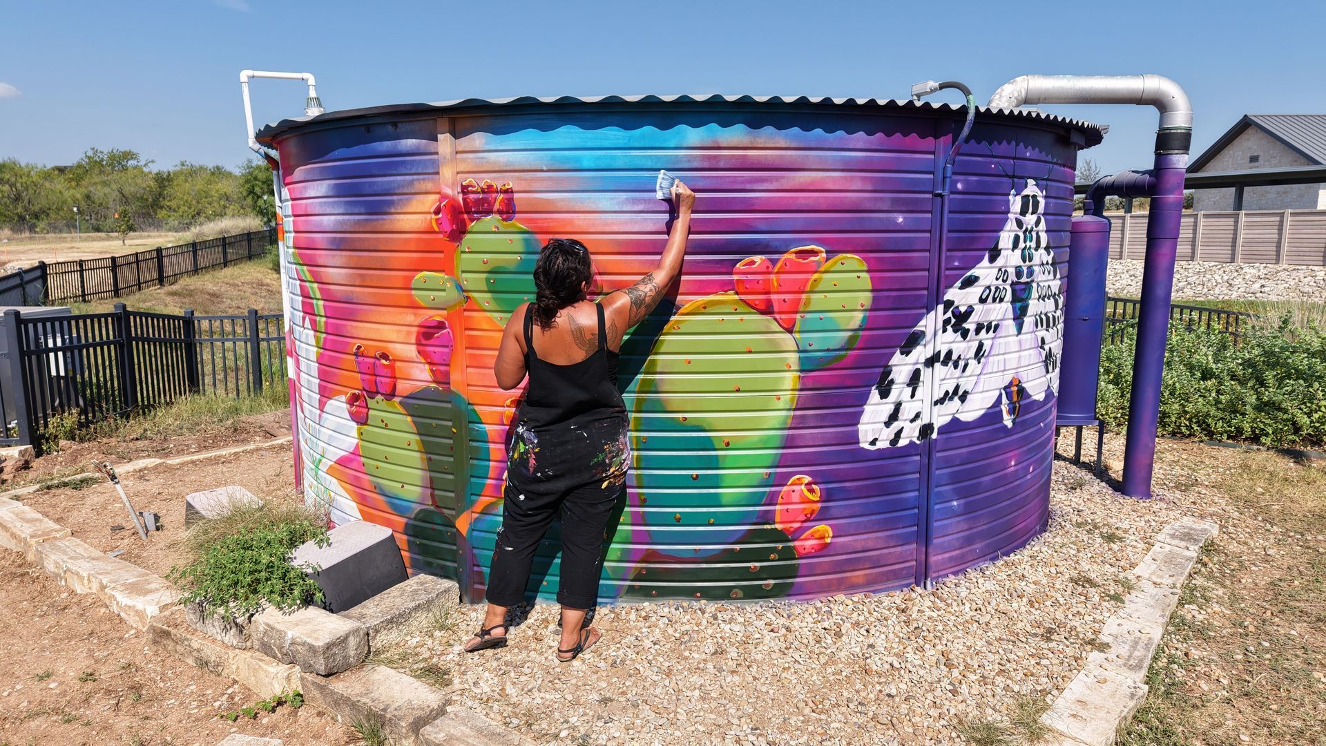 Person painting a colorful mural on a purple water tank outdoors
