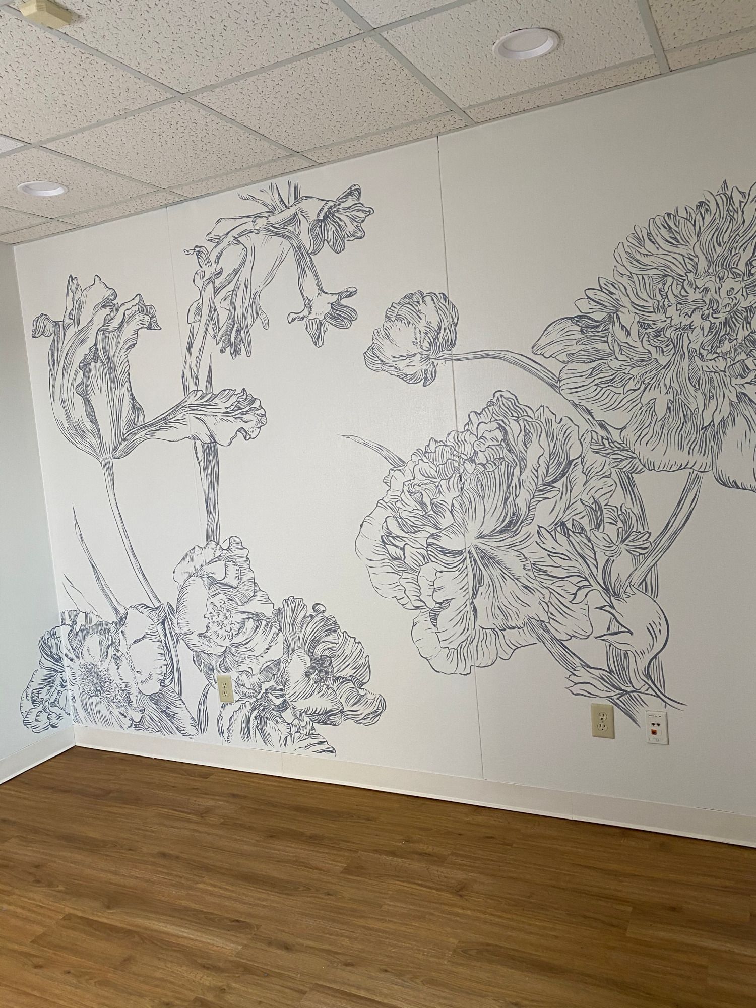Floral line art mural on a white wall in a room with wood flooring.