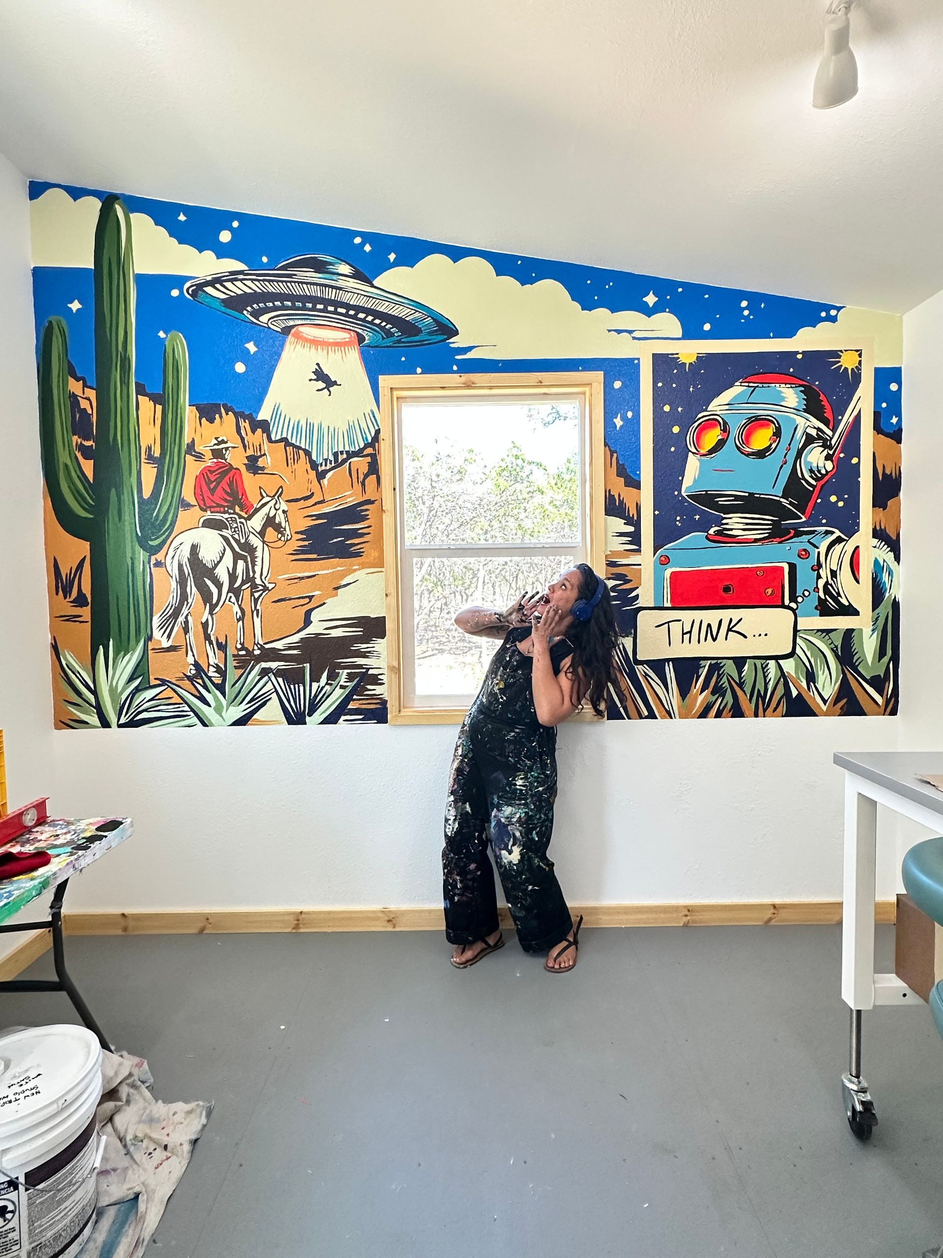 Person standing in a colorful mural-painted room, facing a window in the center wall.
