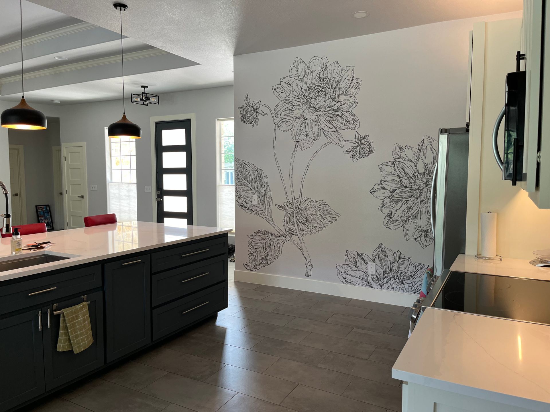 Modern kitchen with dark gray island and white countertops; floral wall art.