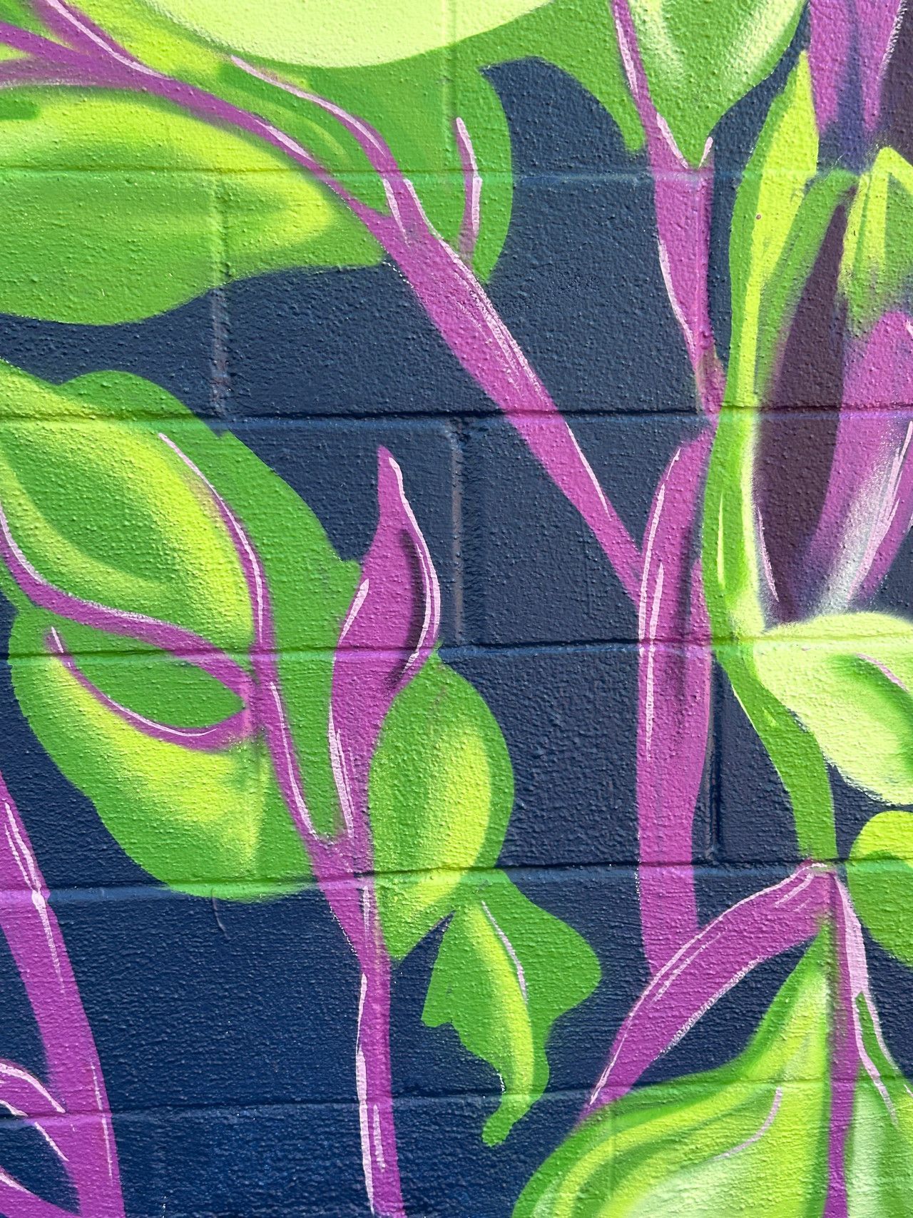 Green and yellow painted leaves and purple stems on a dark blue brick wall.