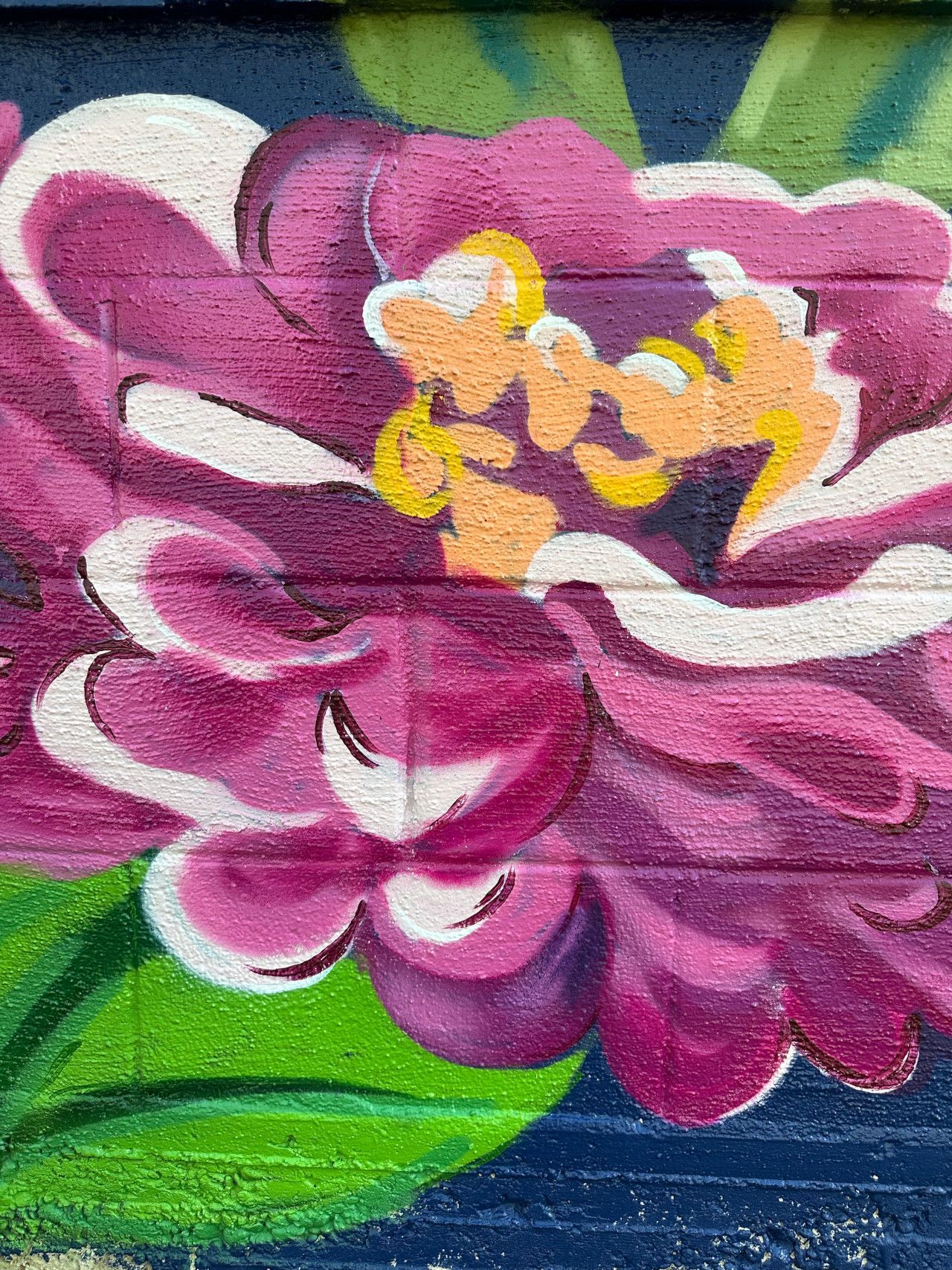Close-up of a vibrant purple and white flower painted on a brick wall; yellow center, green leaves.