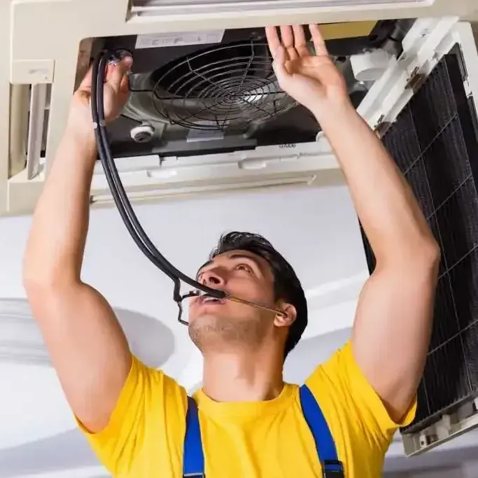 A man in a yellow shirt is working on an air conditioner