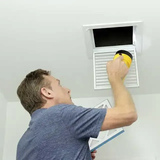 A man is cleaning a vent on the ceiling.