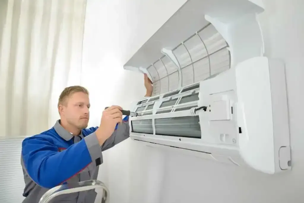 A man is fixing an air conditioner with a screwdriver.