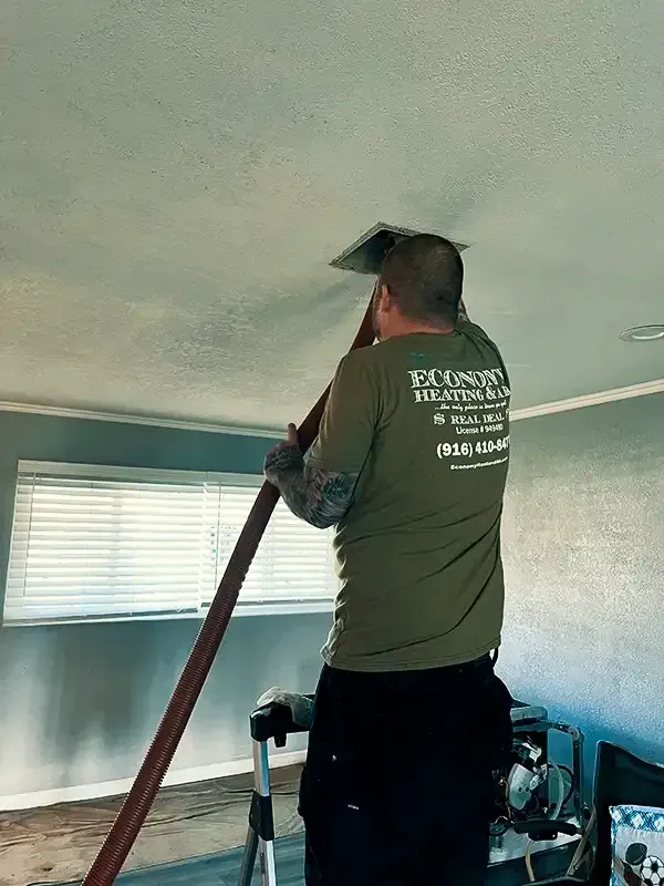A man is cleaning the ceiling of a living room with a vacuum cleaner.
