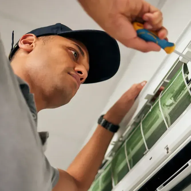 A man wearing a hat is working on an air conditioner