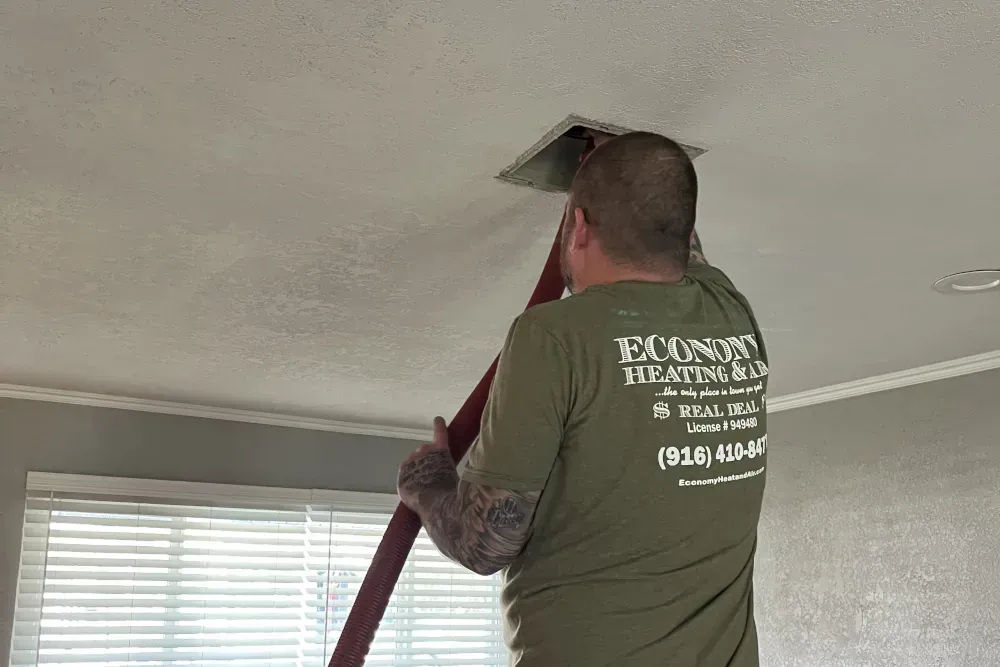 A man in a green shirt is cleaning a vent on the ceiling.