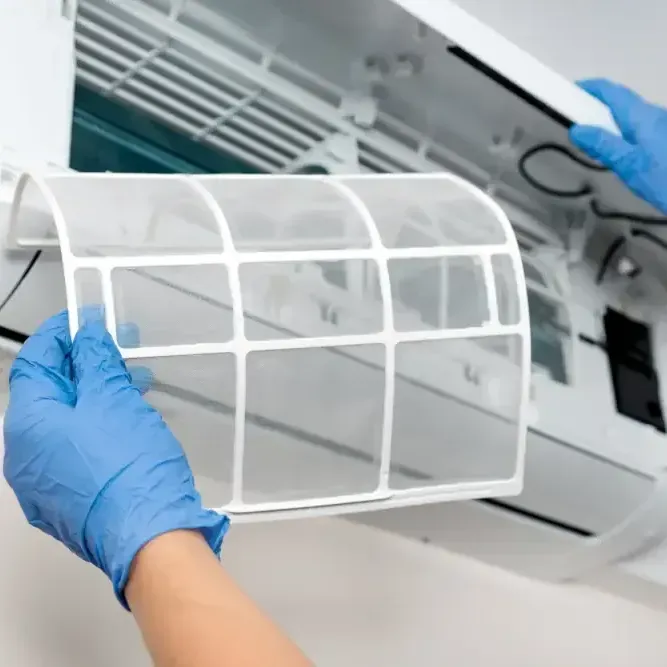 A person wearing blue gloves is cleaning an air conditioner filter.