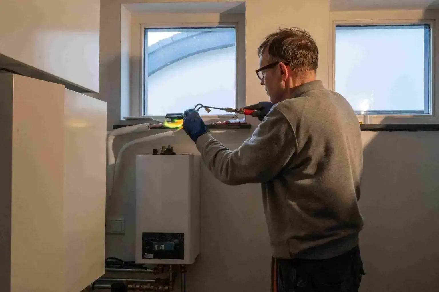 A man is fixing a boiler with a screwdriver in a room.