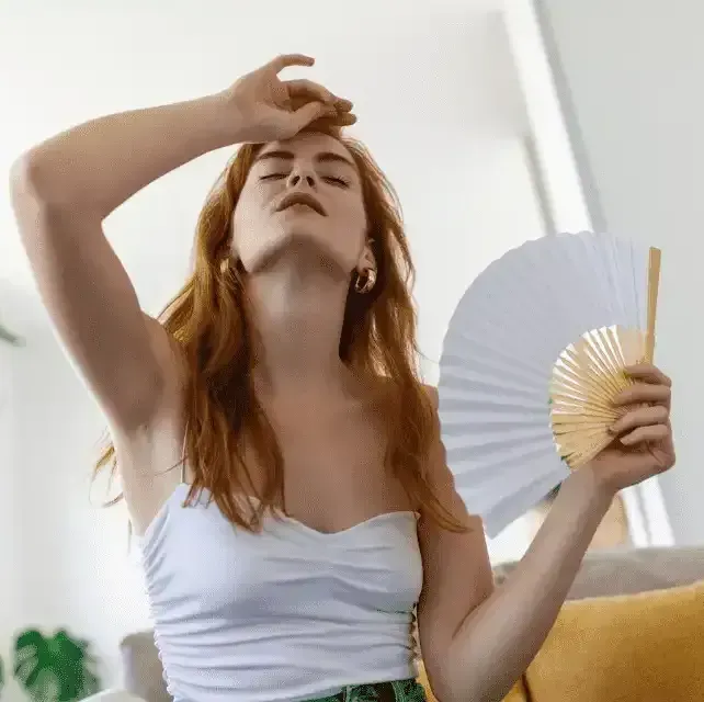 A woman is sitting on a couch holding a fan.