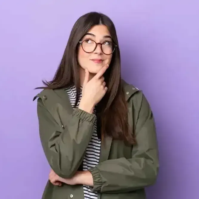 A young woman wearing glasses and a green jacket is thinking.