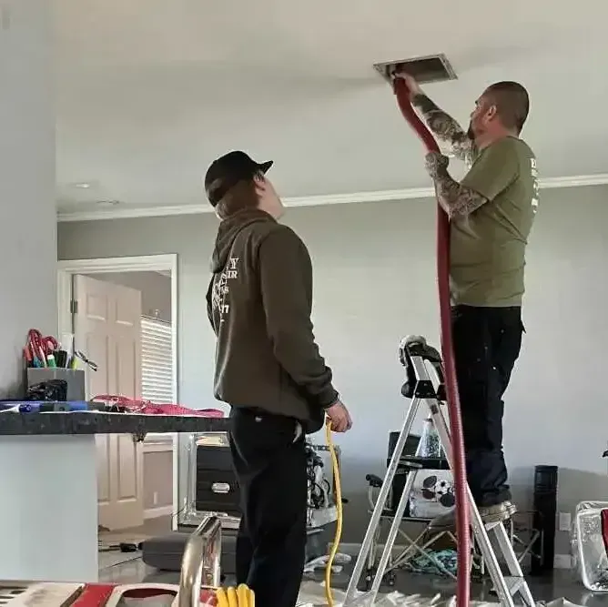 Two men are working on a ceiling in a living room
