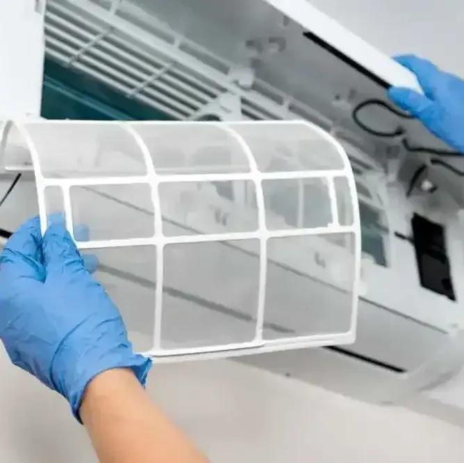 A person wearing blue gloves is cleaning the filter of an air conditioner.