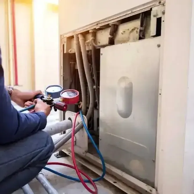 A man is working on a refrigerator with a gauge attached to it.