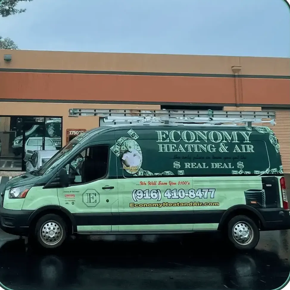 A green economy heating and air van is parked in front of a building