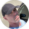 A man wearing a baseball cap is standing next to a car.