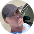 A man wearing a baseball cap is standing next to a car.