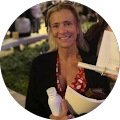 A woman is smiling while holding a cup of coffee and a piece of paper.