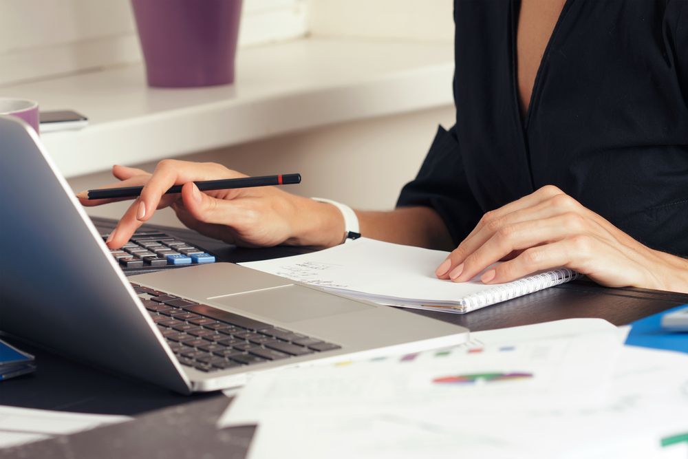A Woman is Sitting at a Desk Using a Laptop and a Calculator — AJA Bookkeeping Services In Cairns, QLD