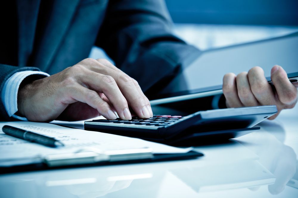 A Person in Suit Using a Calculator, Papers and Pen on a Desk — AJA Bookkeeping Services In Weipa, QLD
