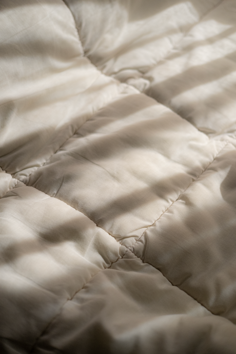 Tejido acolchado color beige con suaves patrones de luz y sombra.