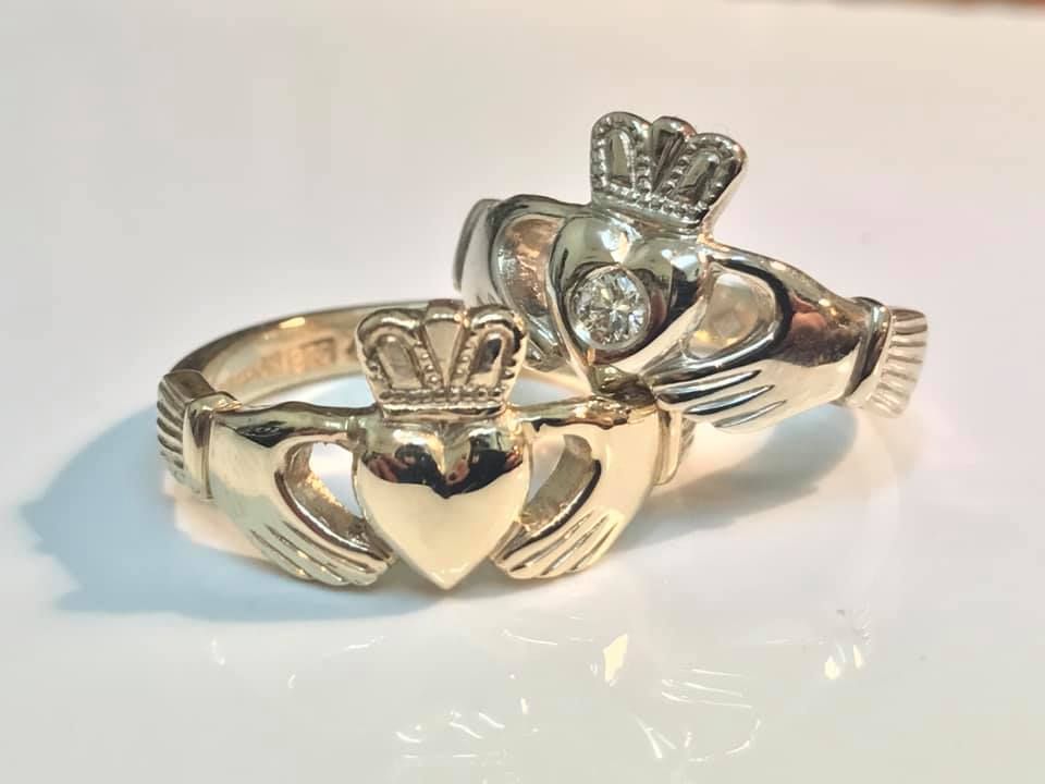 Two gold-toned Claddagh rings resting on a white surface, one featuring a small center diamond — Burchell's Jewellers In Bowral, NSW