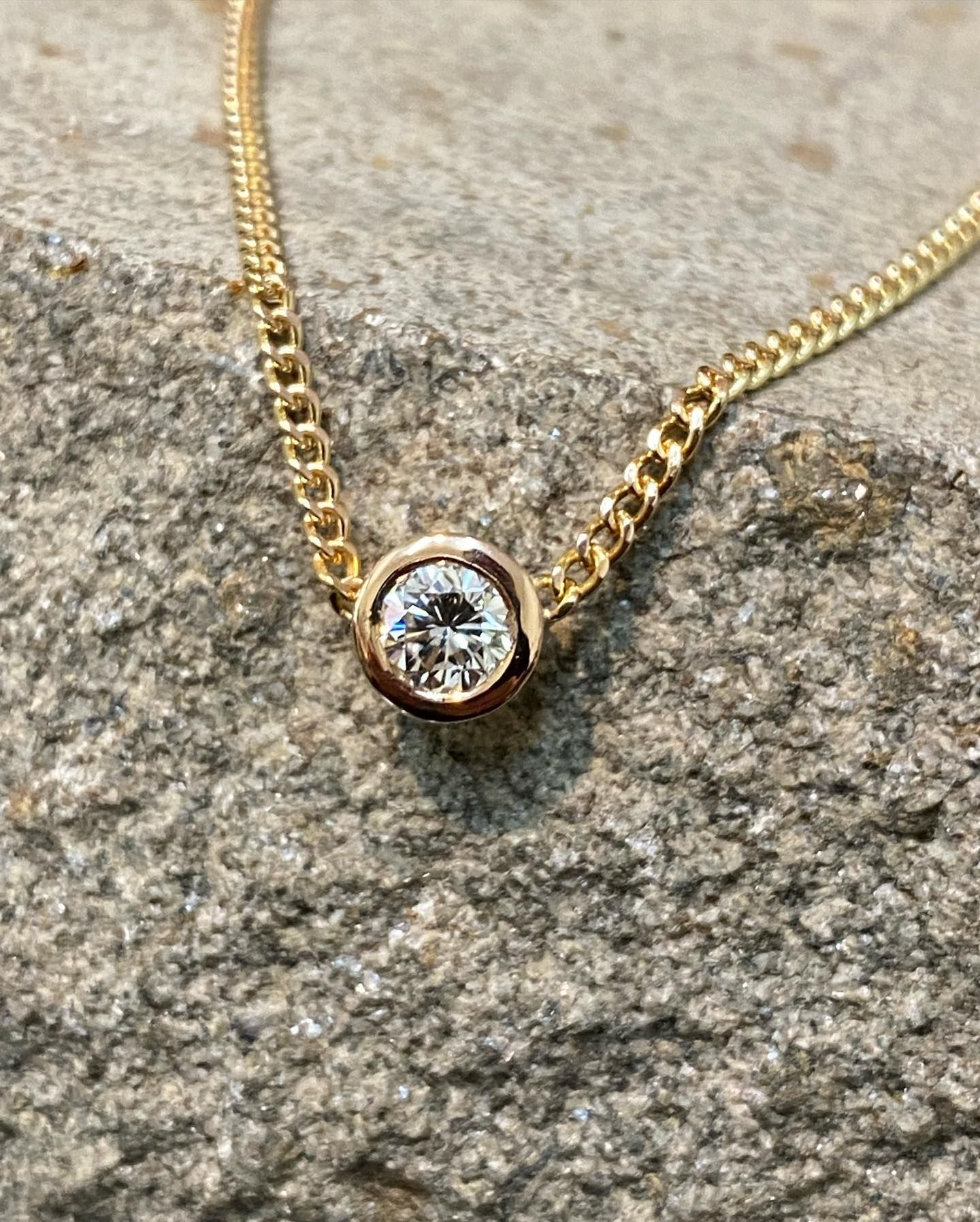 Gold Necklace With a Diamond Pendant on a Rough, Grey Stone Surface — Burchell's Jewellers In Canberra, NSW
