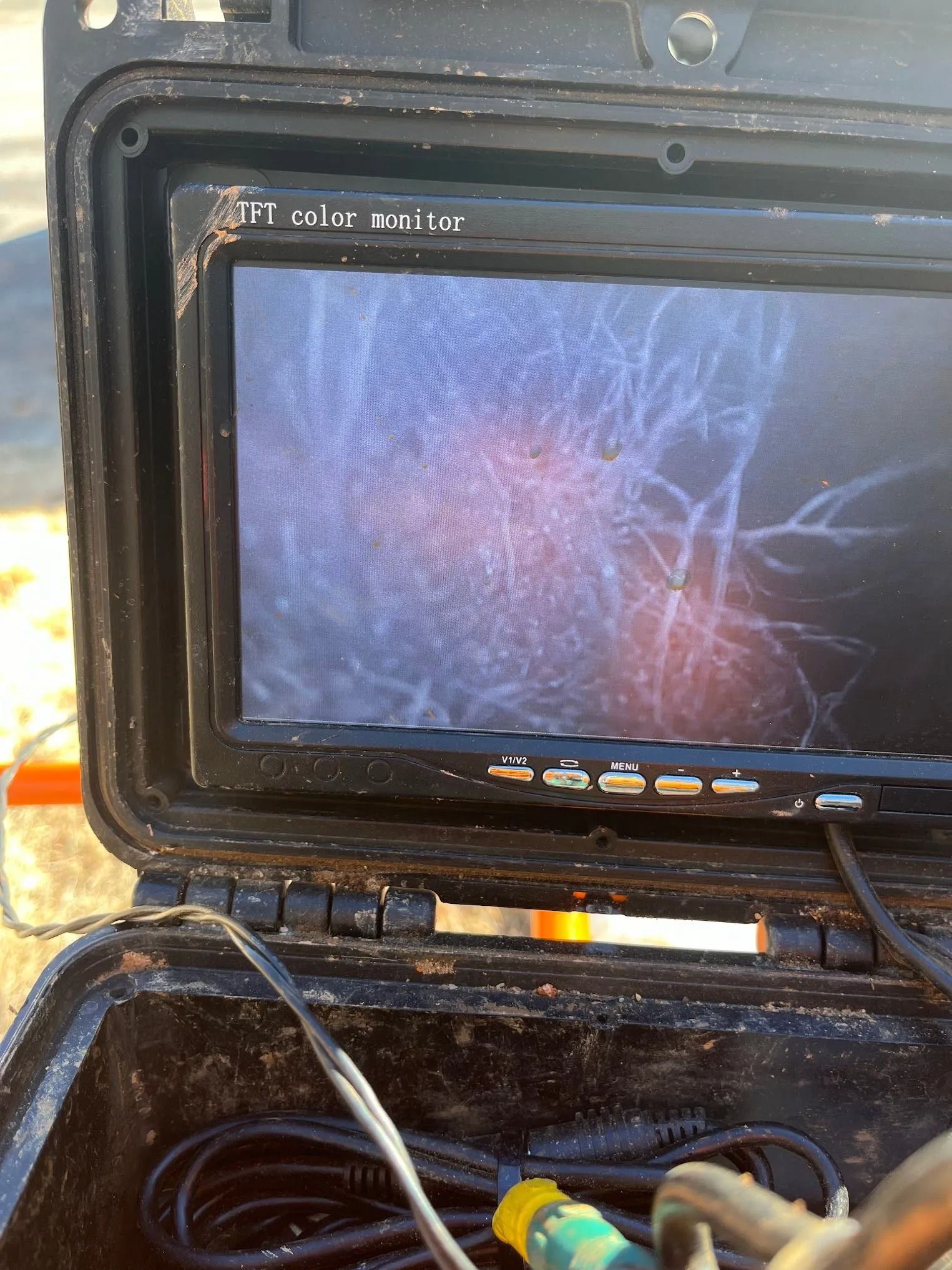 Portable inspection monitor showing a close-up of tangled roots or branches on a screen in a toolbox case