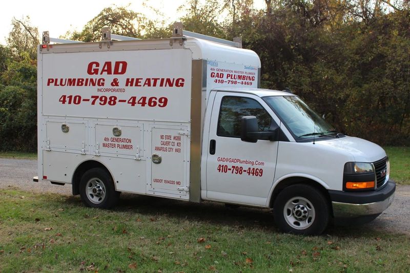White G&D Plumbing & Heating service van parked on grass beside trees in daylight