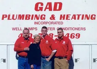 Three people in red shirts standing before a GAD Plumbing & Heating company sign