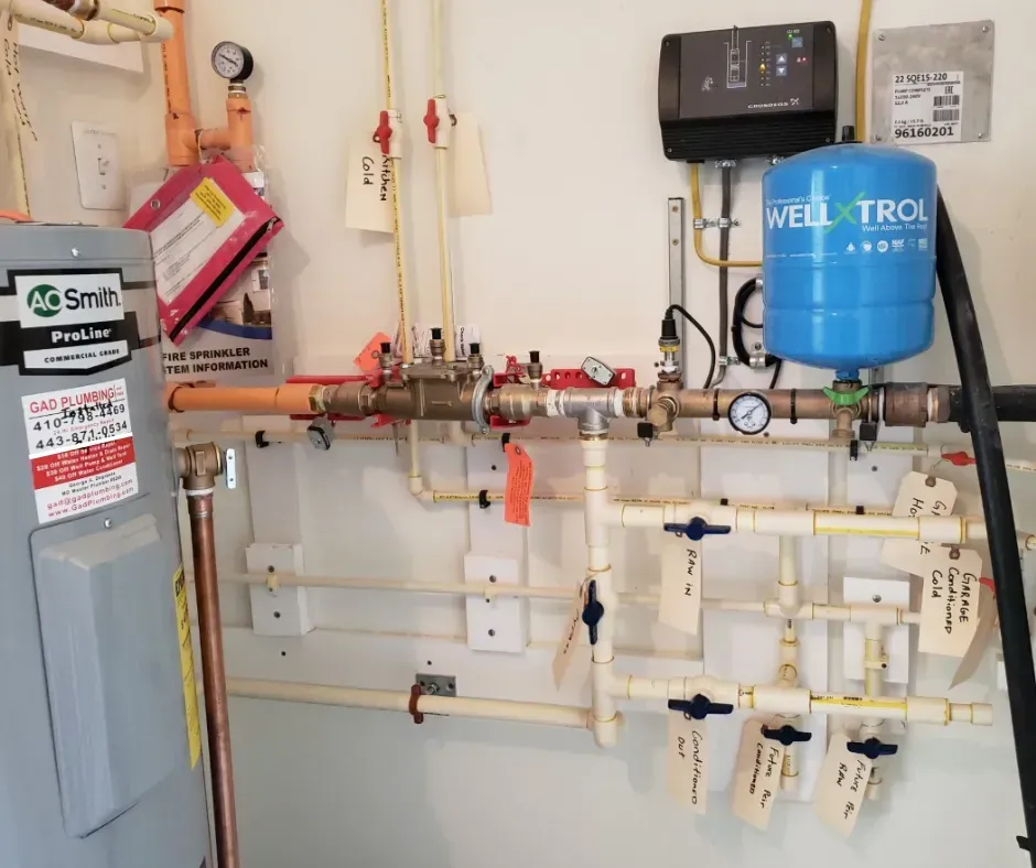 Wall-mounted plumbing and filtration equipment with gauges, valves, and blue water tank in a utility room