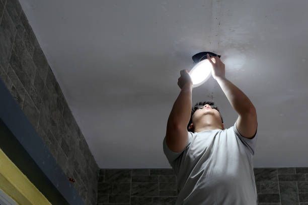 Person installing a ceiling light while standing in a tiled room