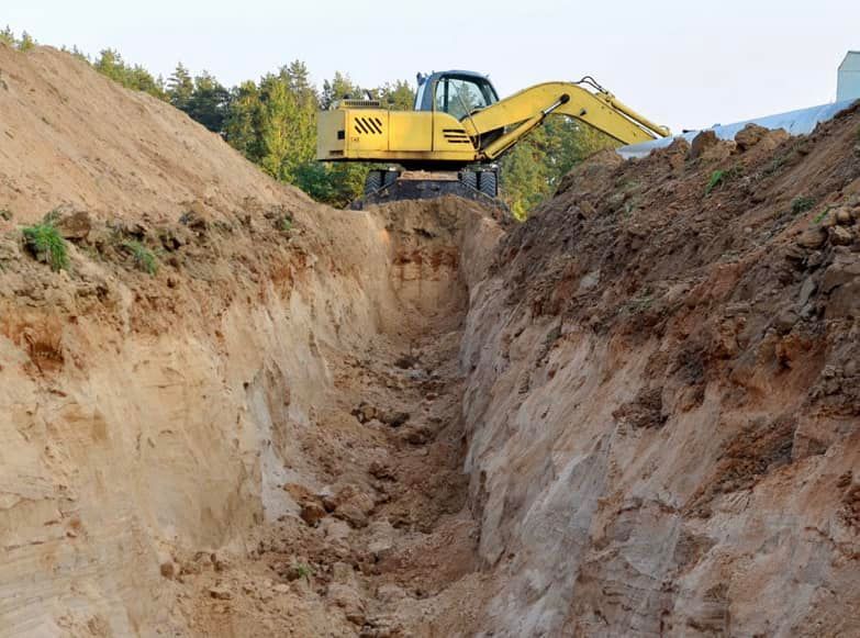 A yellow excavator is digging a trench in the dirt.