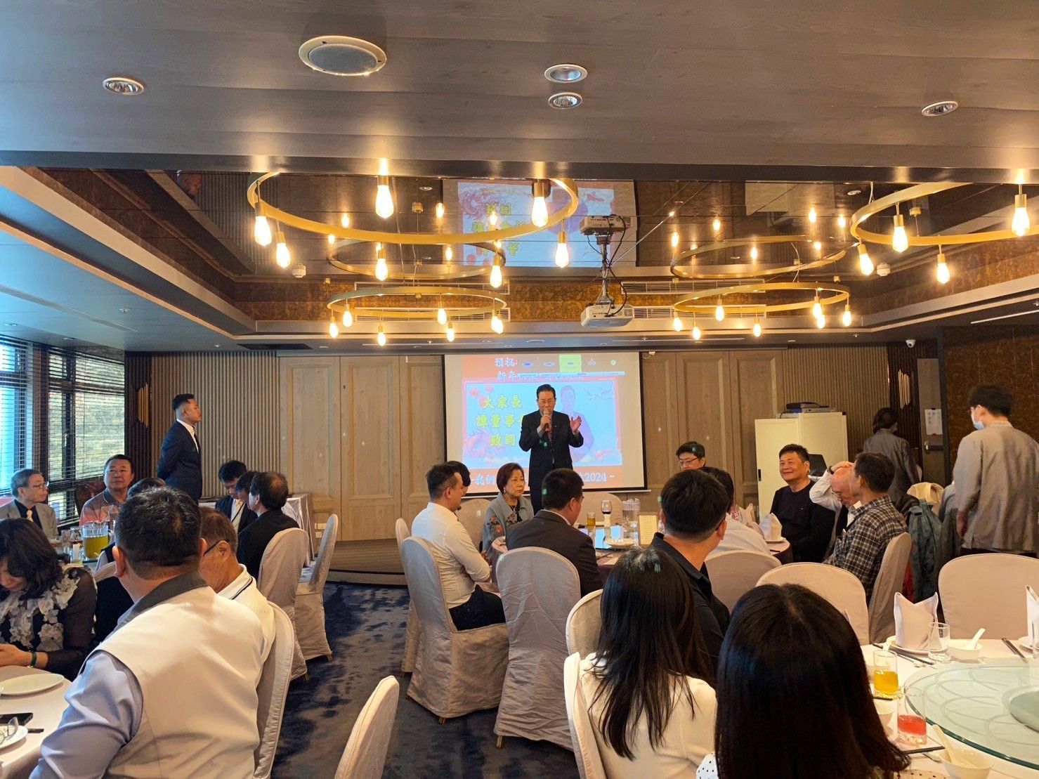 會議晚宴上,與會者圍坐在圓桌旁,演講者在台上發表演說。