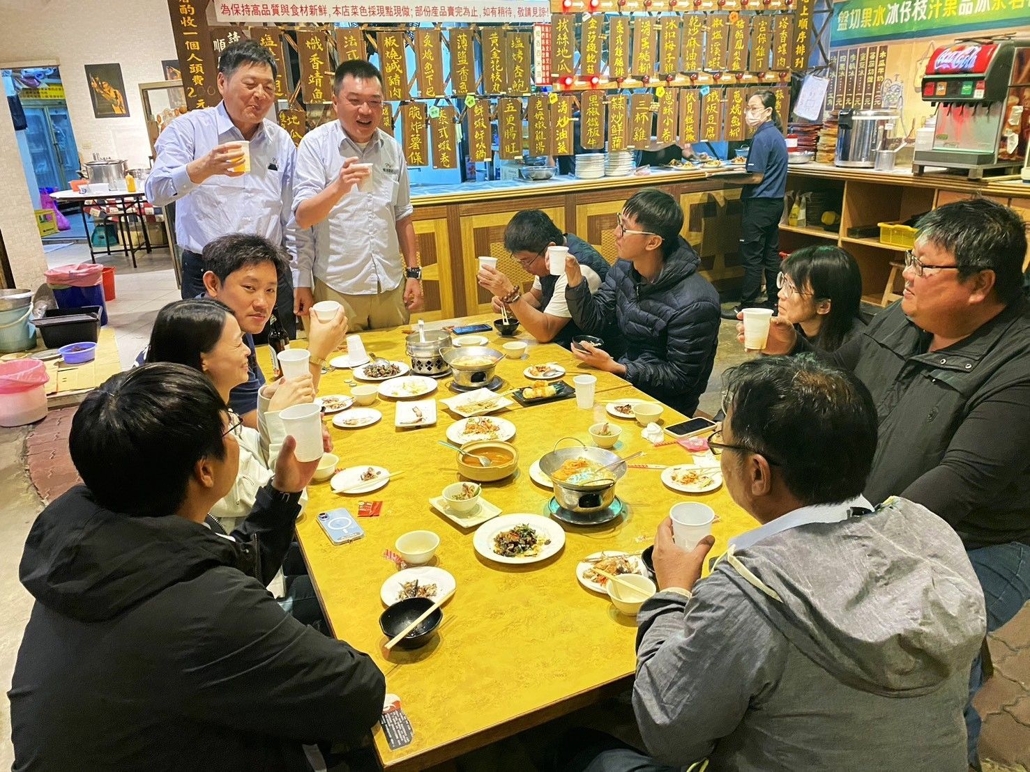 人們在熱鬧的餐廳餐桌旁用餐、舉杯慶祝,餐桌上擺滿了菜餚和飲料。