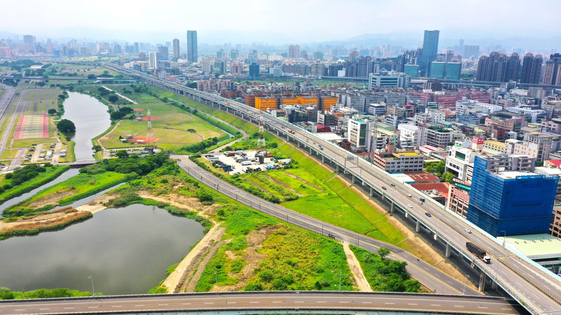 薄霧籠罩下的城市鳥瞰圖，蜿蜒的河流、綠意盎然的公園、高速公路和密集的城市天際線盡收眼底。