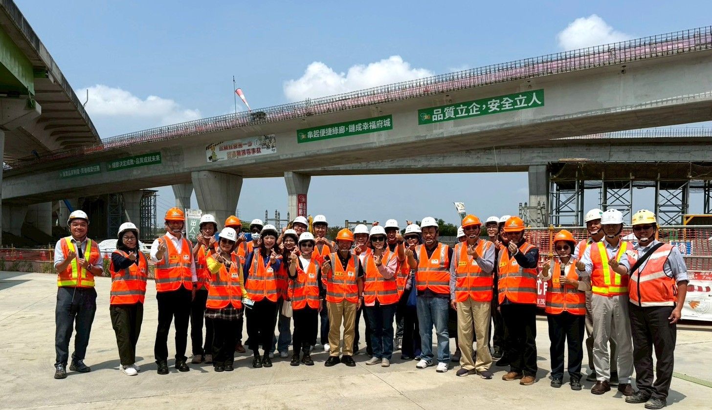 身穿橙色安全背心、頭戴安全帽的建築工人在正在建設中的高速公路立交橋上擺姿勢拍照
