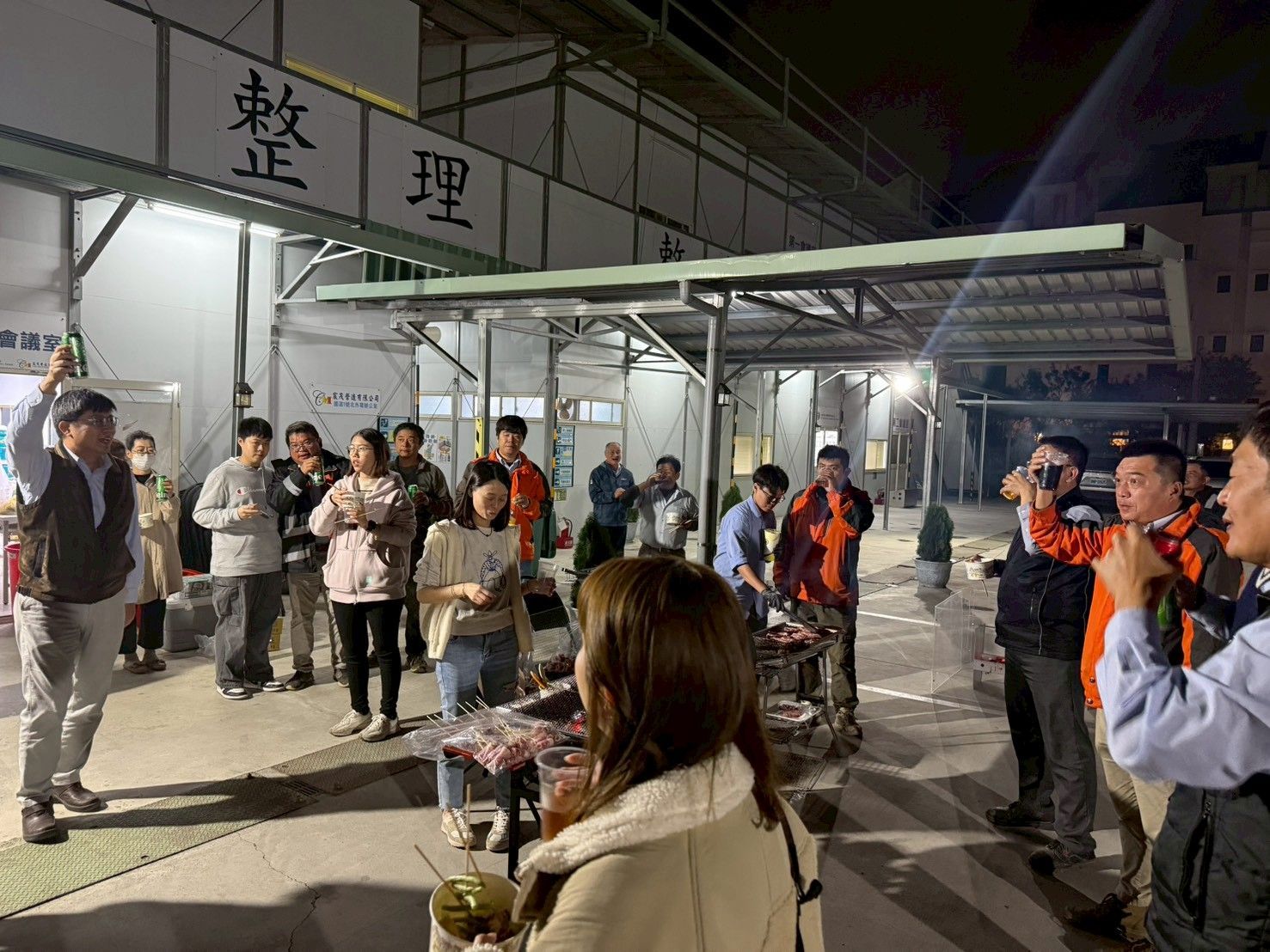 夜裡,人們聚集在一棟建築物外,有些人穿著橘色安全背心,靠近一塊寫著「整理」的標誌。