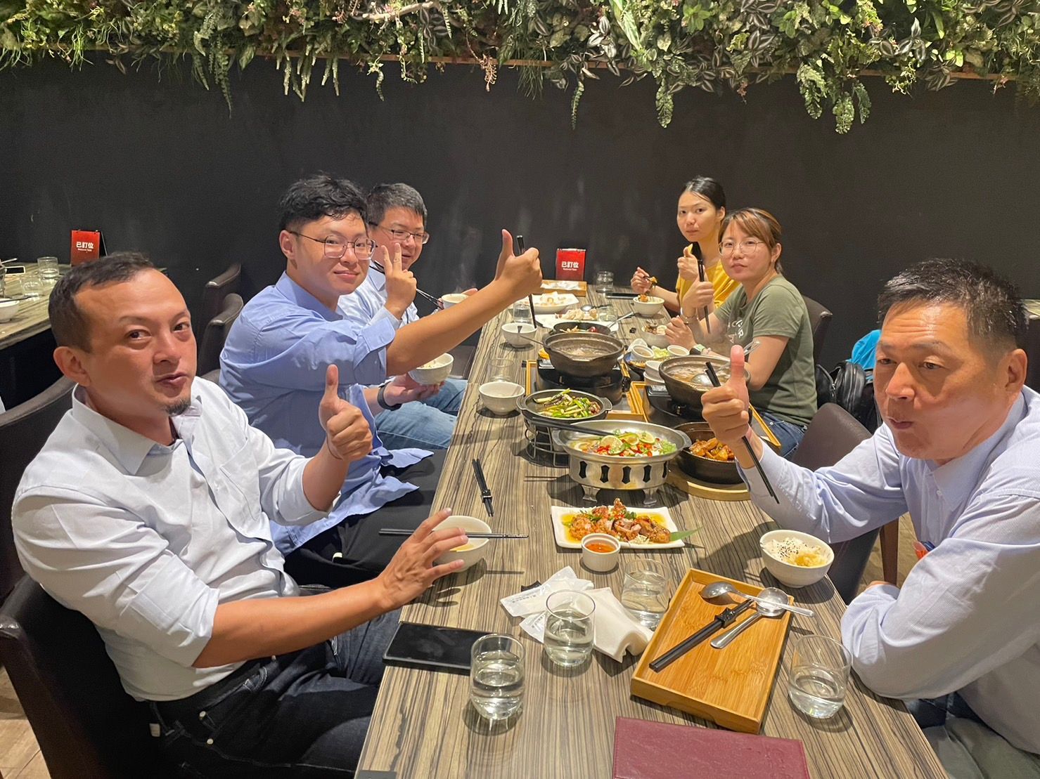 一群人在戶外長桌旁用餐，舉杯隨意碰杯。