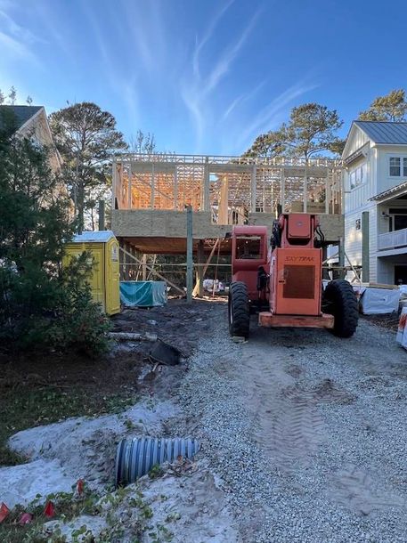 Construction site; wooden framing of a building; orange forklift; portable toilet; trees.