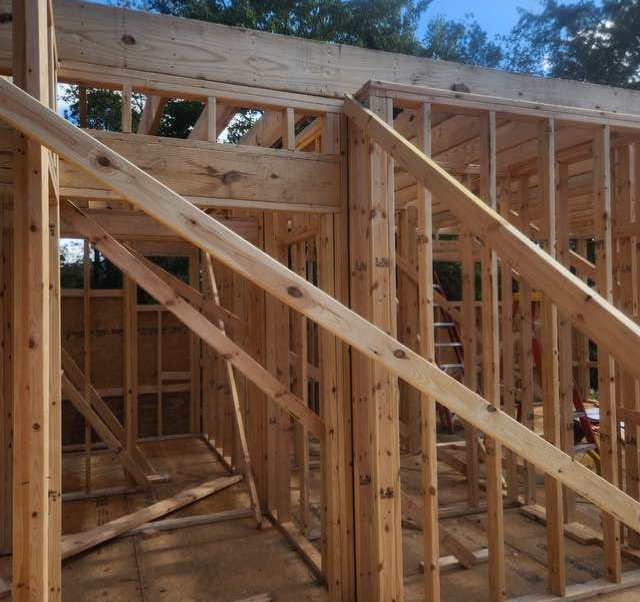 Wooden frame of a building under construction, showing walls and roof supports, outdoors.