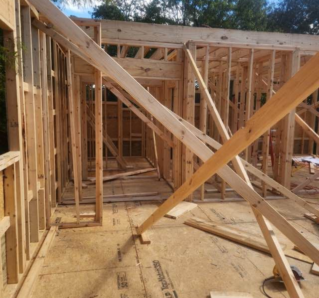 Wooden frame of a building under construction, showing walls, doorway, and support beams.