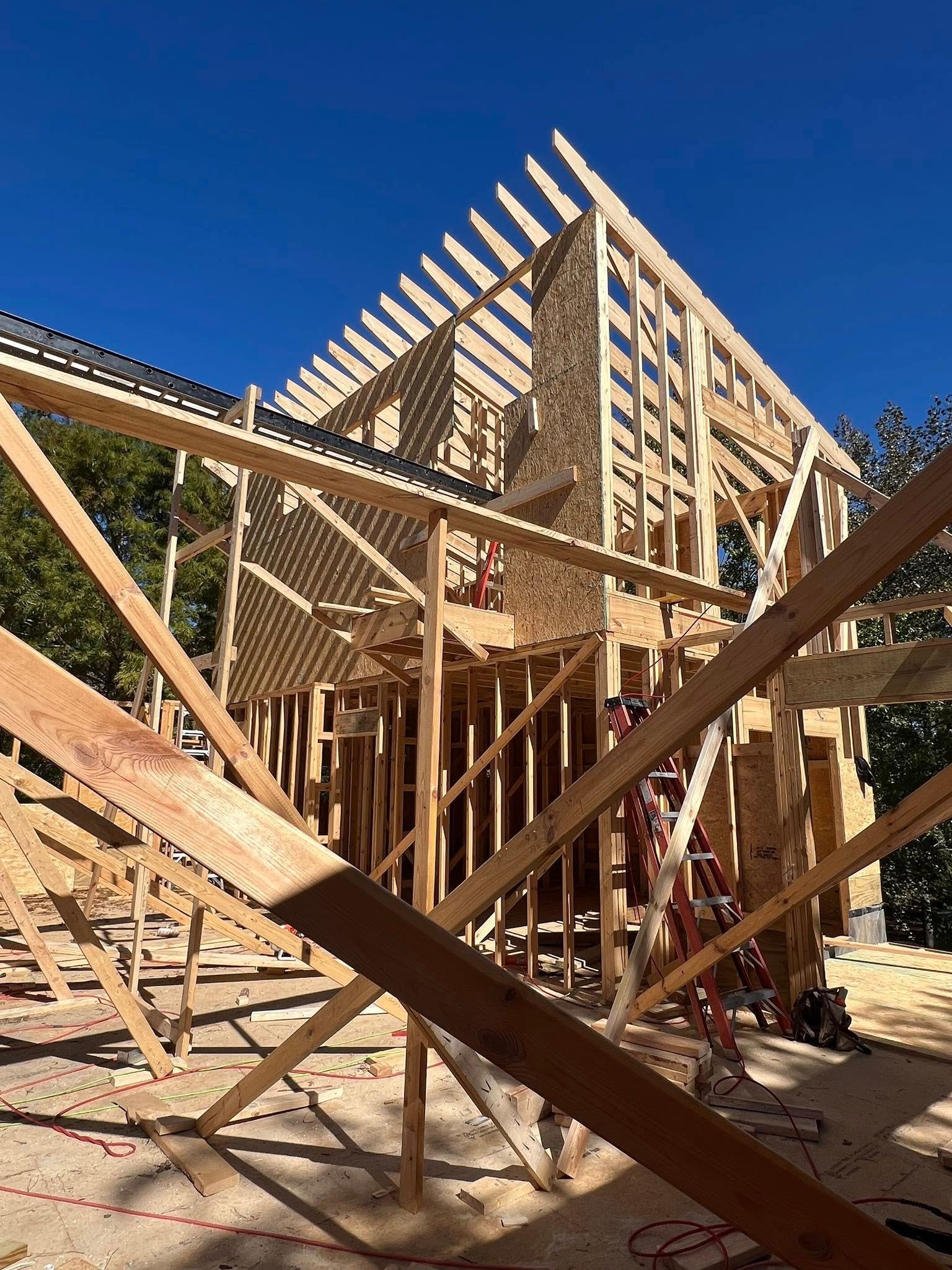 Wooden frame of a house under construction against a clear blue sky.