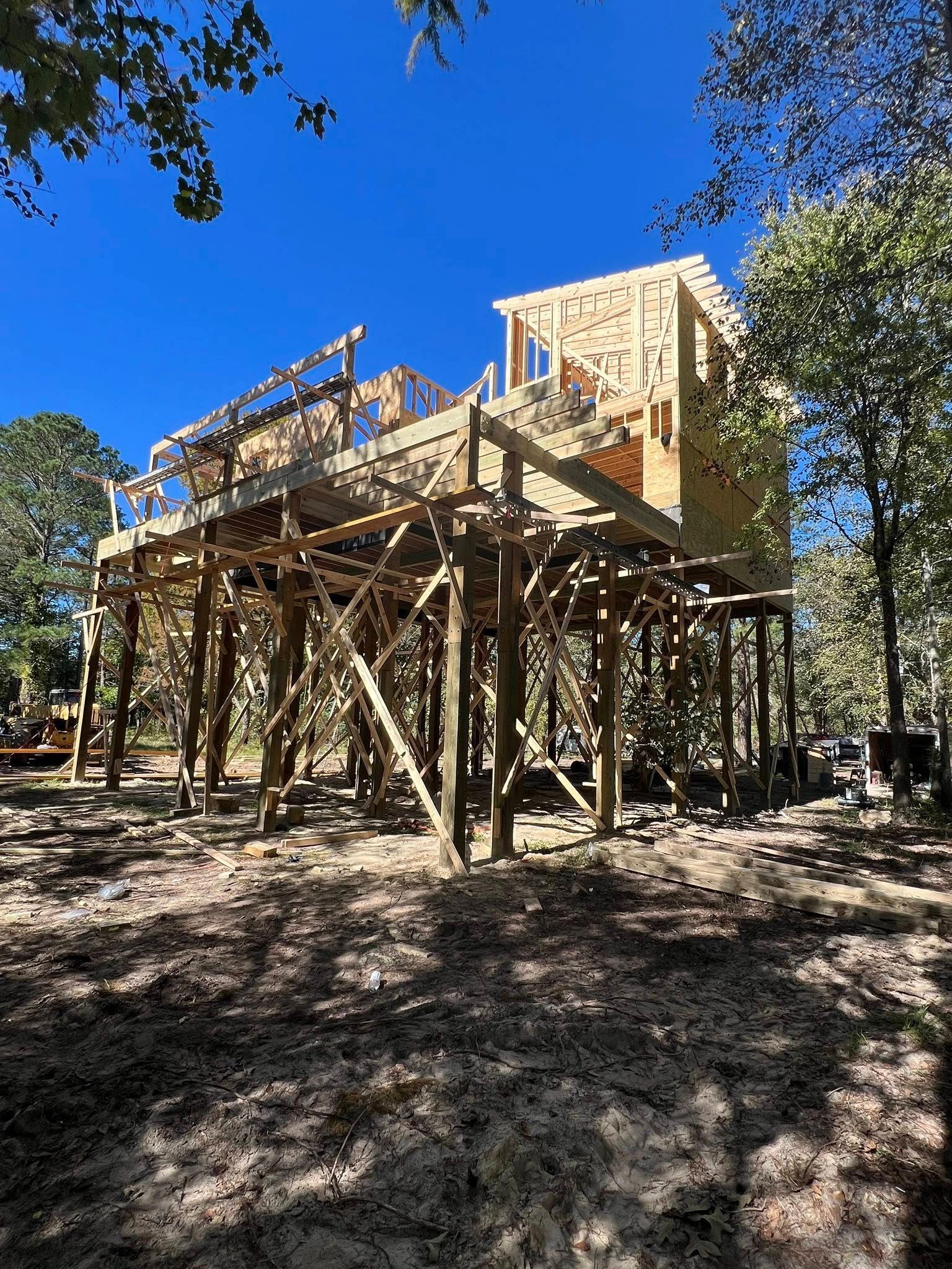 A wooden structure under construction, elevated on stilts against a clear blue sky.