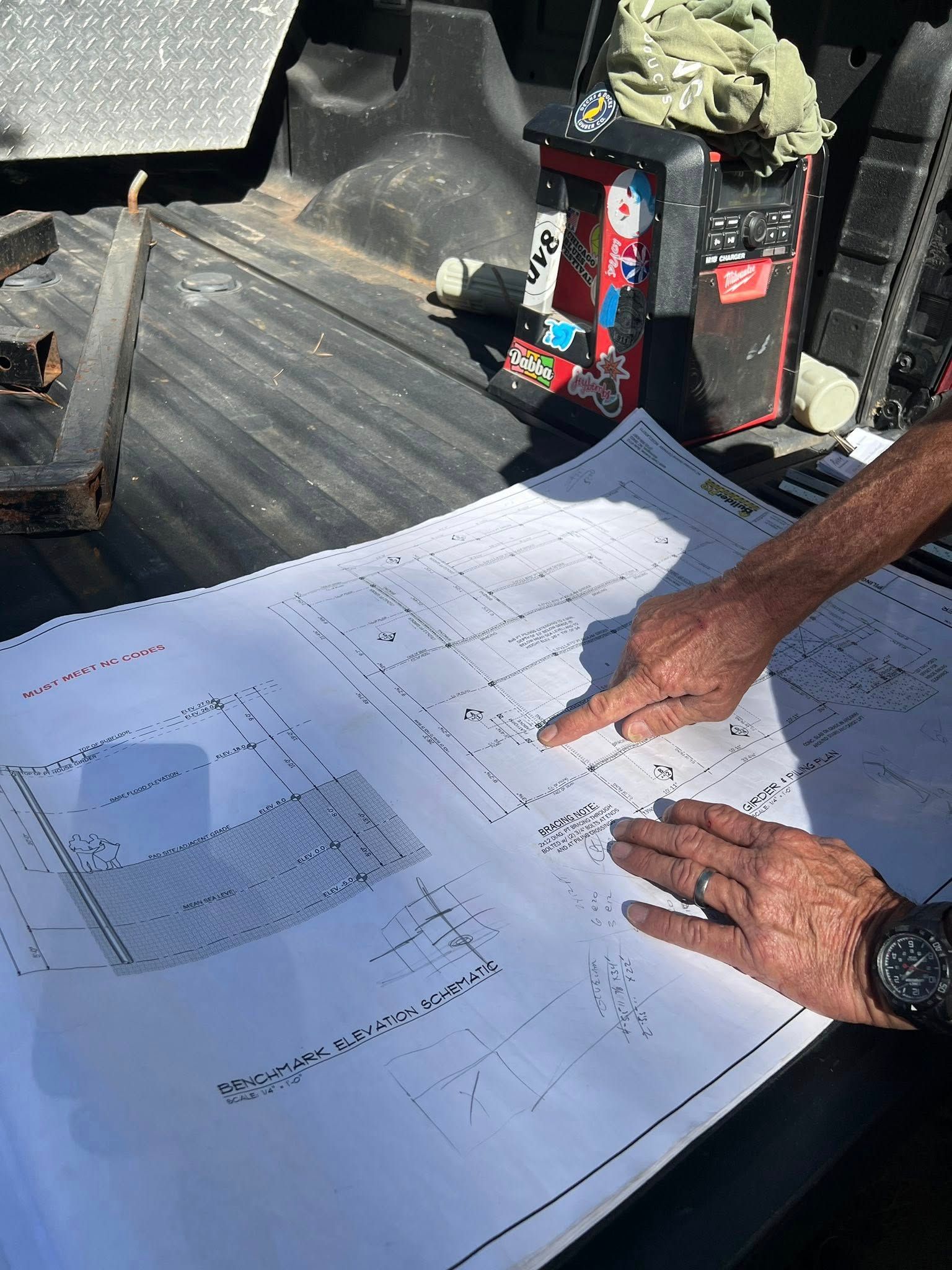 Two hands pointing at architectural plans on the bed of a truck.
