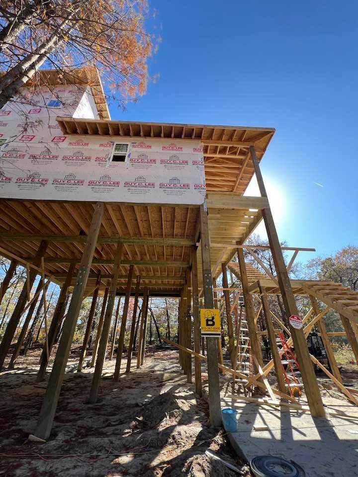 Elevated wooden structure under construction, with high stilts and partially covered with protective wrap