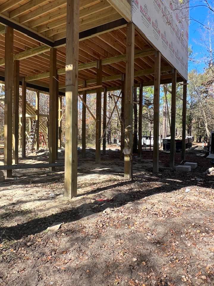 Wooden deck under construction, elevated on posts above ground.