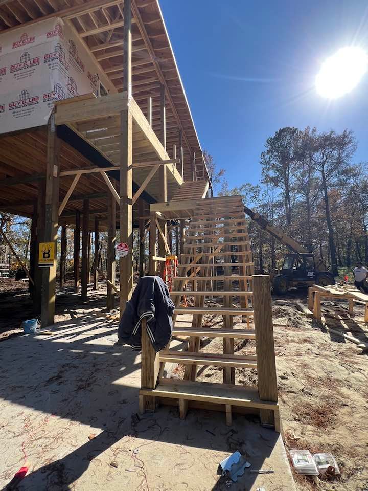 Wooden staircase leading to a partially built elevated structure on a sunny day.